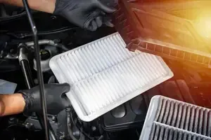 Mechanic holding a dirty cabin air filter beside a clean replacement in a car engine bay