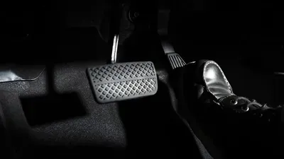 Foot pressing a car pedal in a dark interior, with a sneaker on the accelerator.