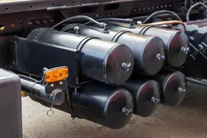 Row of black metal tanks or cylinders mounted on a vehicle chassis with orange fittings
