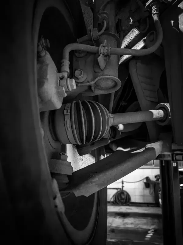 Black-and-white close-up of a vehicle’s suspension and CV axle wheel assembly underneath.