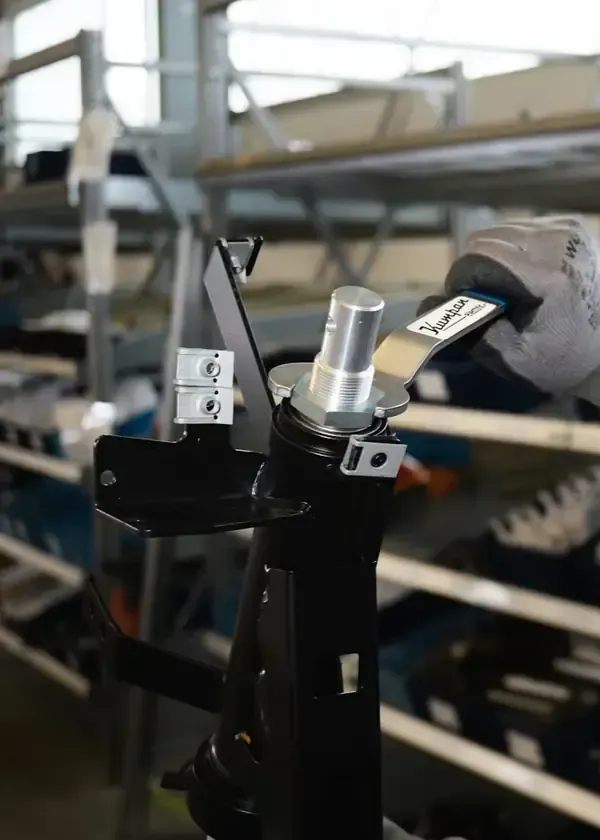 Gloved worker adjusts a metal part on an industrial machine in a workshop.