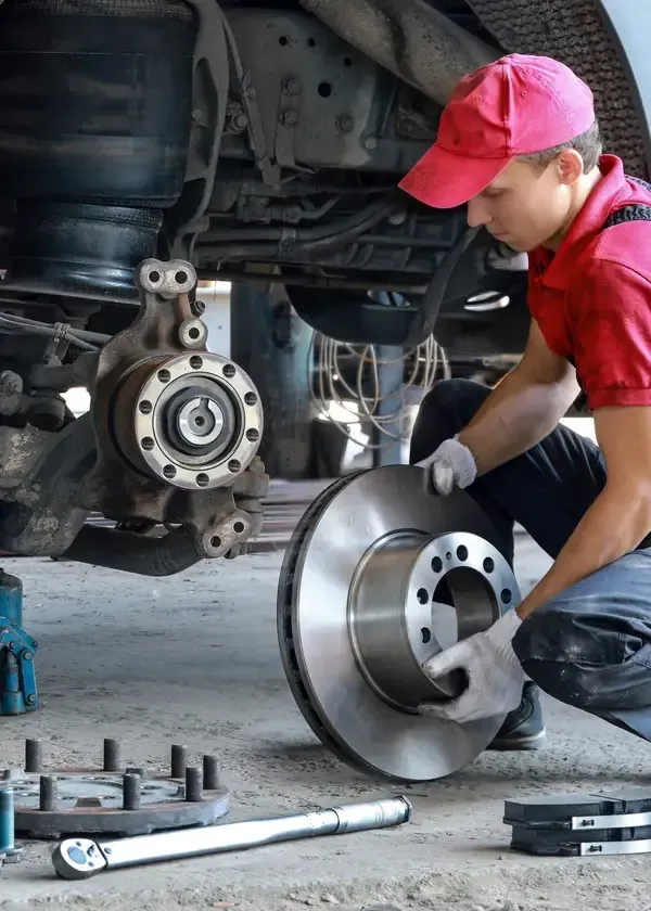 Mechanic in red cap installing a brake rotor on a car in a garage