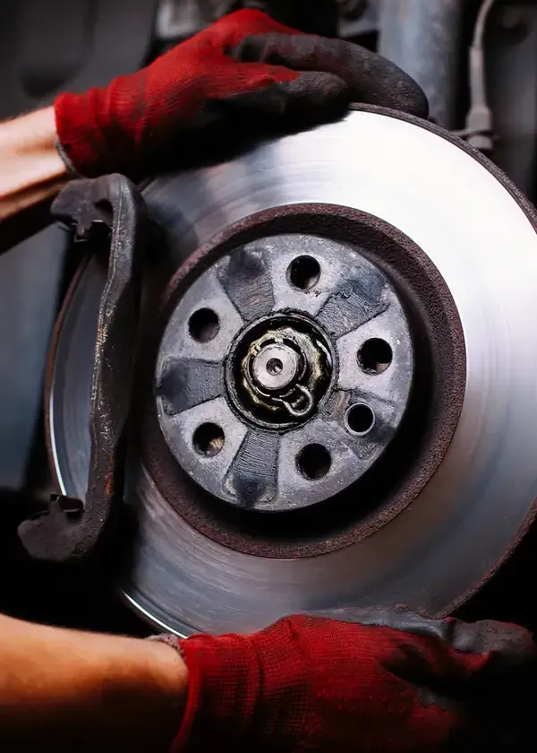 Gloved hands replacing a car brake rotor with brake caliper visible