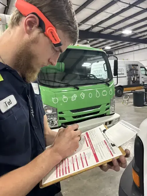 Mechanic in red-and-black uniform using a diagnostic tablet inside a car