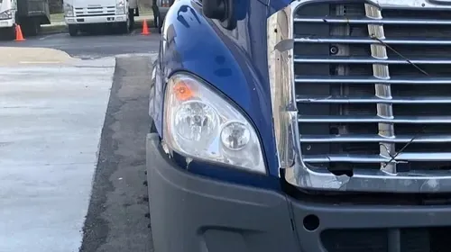 Close-up of a red truck’s front headlight and grille inside a garage or warehouse