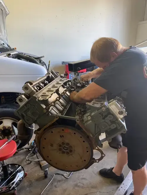 Person working on a large engine in a garage, leaning over the exposed machinery.