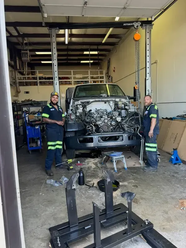 Two workers in a garage servicing a vehicle with a heavily damaged front end