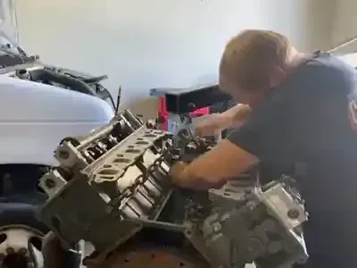 Mechanic leaning over a car engine, working in a garage with engine parts visible