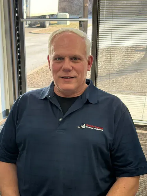 Man seated indoors by a window, wearing a navy polo shirt with a logo, looking at the camera.