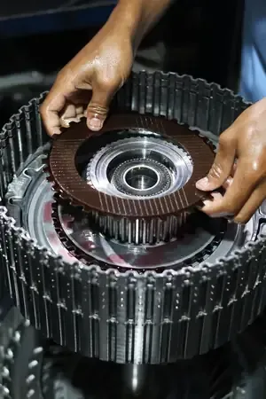 Hands positioning a metal gear inside a large industrial machine assembly.