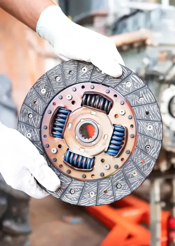 Gloved hands holding a car clutch disc with visible blue springs in a workshop