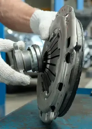 Gloved hands inspect a silver automotive clutch disc on a workbench