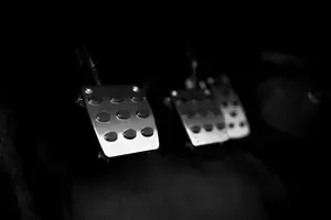 Two metal car pedals in a dark interior, lit with a bright reflection