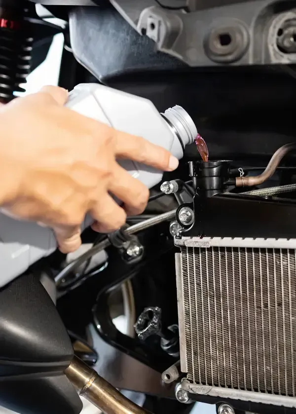 Hand pouring coolant into a motorcycle radiator fill cap.