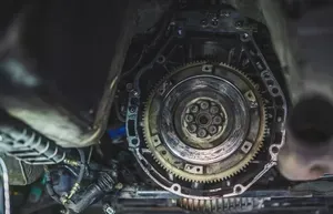 Close-up of a mechanical engine flywheel and surrounding components inside a dimly lit vehicle compartment