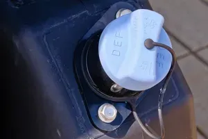 Close-up of a white fuel cap on a dark blue vehicle body, with a tether attached.
