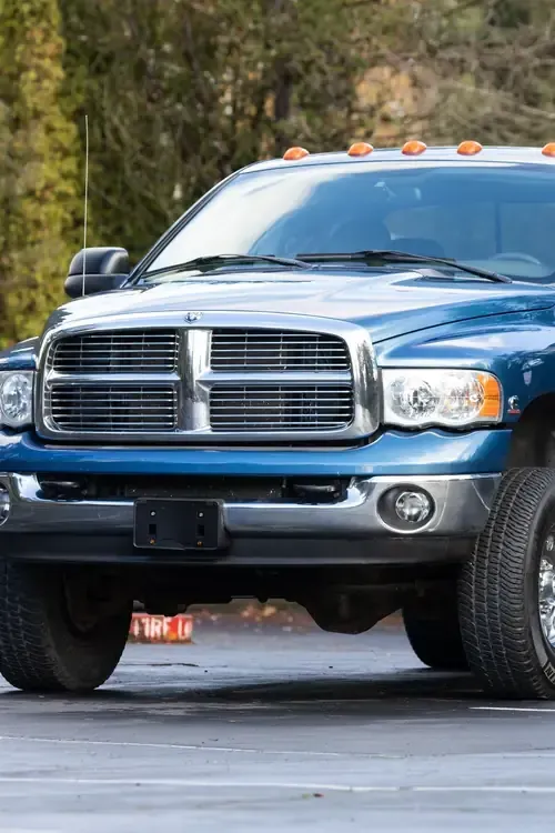 Blue pickup truck parked on pavement, front view, with amber cab lights and trees in the background