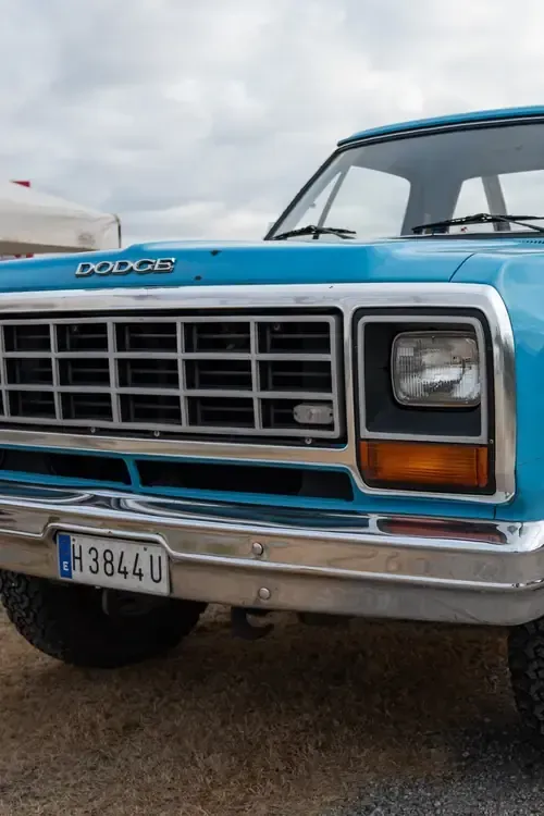 Close-up of a blue vintage Dodge truck front grille and headlight on a cloudy day