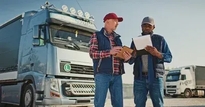 Two truck drivers reviewing paperwork beside a blue semi-truck in a parking lot