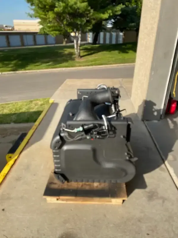 Stacked black equipment on a pallet outdoors beside a building and road.