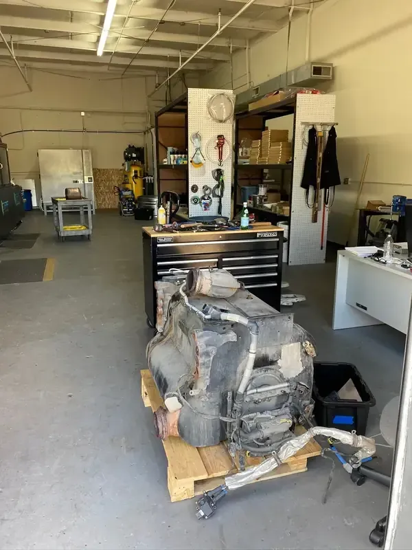 Large workshop with a workbench, tool chests, and a backpack resting on a wooden pallet in the foreground