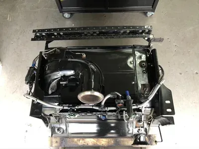 Black car seat assembly with metal frame and tubing on a garage floor, viewed from above