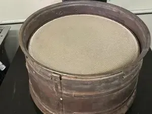 Large round metal sieve or drum with a beige mesh top on a work surface