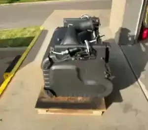 Large black machine or engine on a wooden pallet outdoors beside a curb and building.