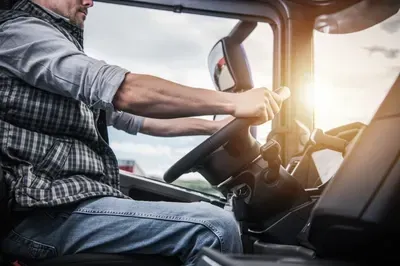 Driver holding steering wheel in a truck cab with sunlight streaming through the window