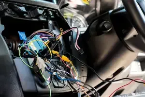 Exposed multicolored wires and connectors inside a car dashboard near the steering wheel.