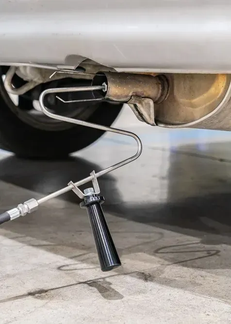 Mechanic using a black-handled exhaust pipe tool under a car in a garage