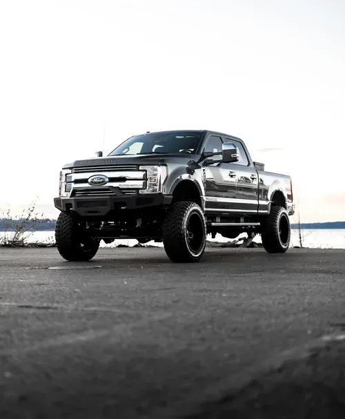 Black lifted pickup truck on a paved road with a bright sky background