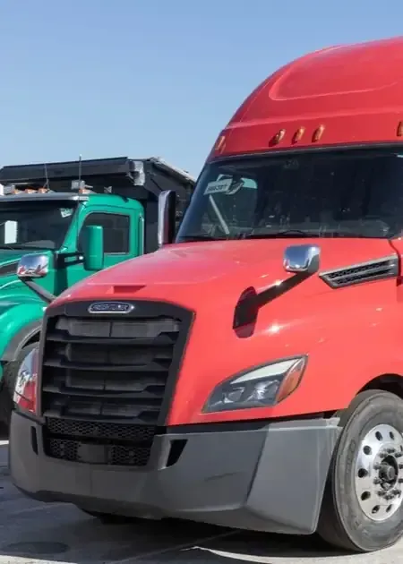 Red semi-truck parked beside a teal truck under a clear blue sky