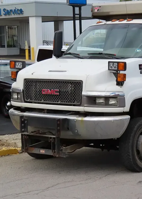 White GMC tow truck with front-mounted equipment parked outside a service station.