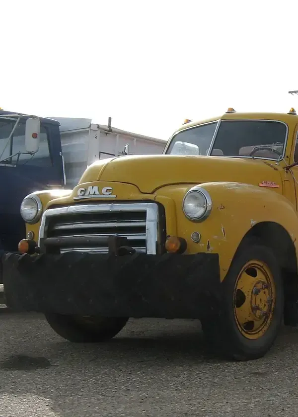 Yellow vintage GMC truck parked outdoors at a junkyard or lot