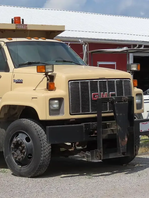 Beige tow truck with a front grille guard parked outdoors near a red building.