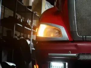 Close-up of a red truck’s front headlight and grille inside a garage or warehouse