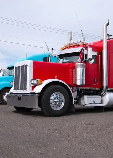 Red semi truck parked on pavement beside a blue truck under a cloudy sky