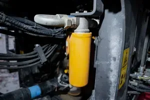 Close-up of a yellow cylindrical filter or reservoir with hoses and wiring in an industrial machine compartment
