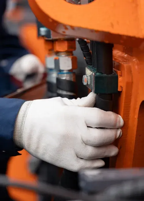 Gloved hand adjusting a bolt on an orange industrial machine