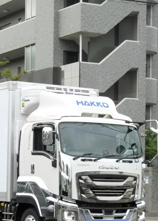 White HAKKO truck parked beside a gray apartment building with exterior stairways