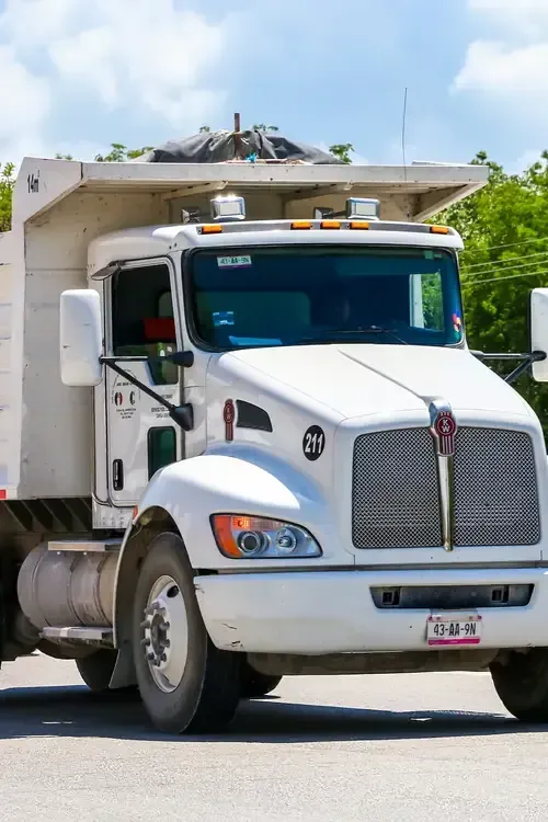 White dump truck driving on a road under a blue sky