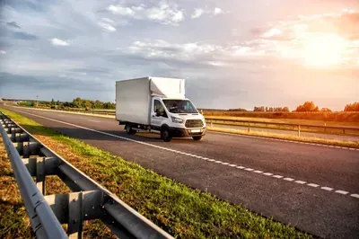 White delivery truck driving on a highway at sunset, with guardrails and open sky