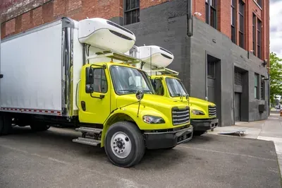 Two yellow box trucks parked on a city street beside a brick building