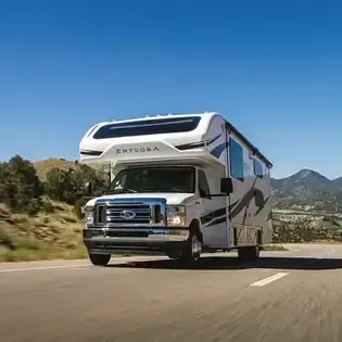 White ENTEGRA RV driving on a road with mountains and blue sky in the background