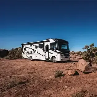 White RV parked on a rocky desert landscape under a clear blue sky.