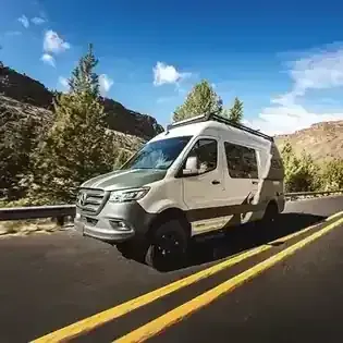 White van driving on a mountain road with double yellow lines under a blue sky
