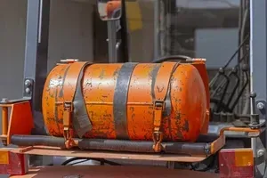 Orange gas cylinder strapped to a trailer rack in an industrial setting