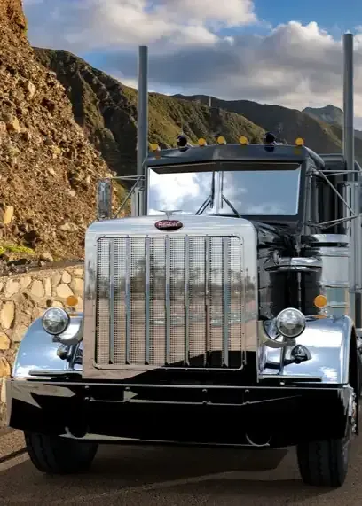 Chrome semi truck driving on a mountain road with rocky cliffs and cloudy sky