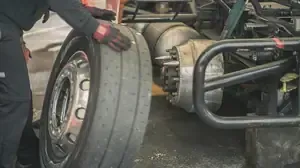 Mechanic changing a large truck tire beside a vehicle chassis in a workshop